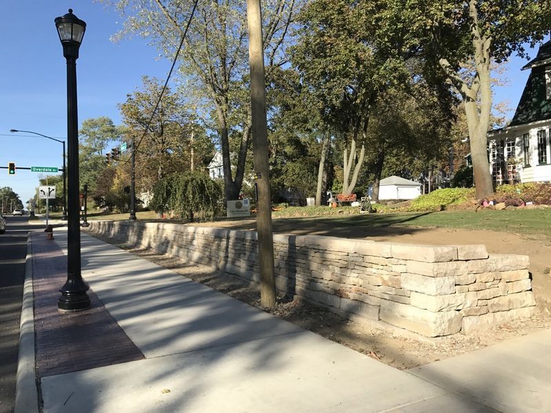 A brick wall along a sidewalk next to a street light.
