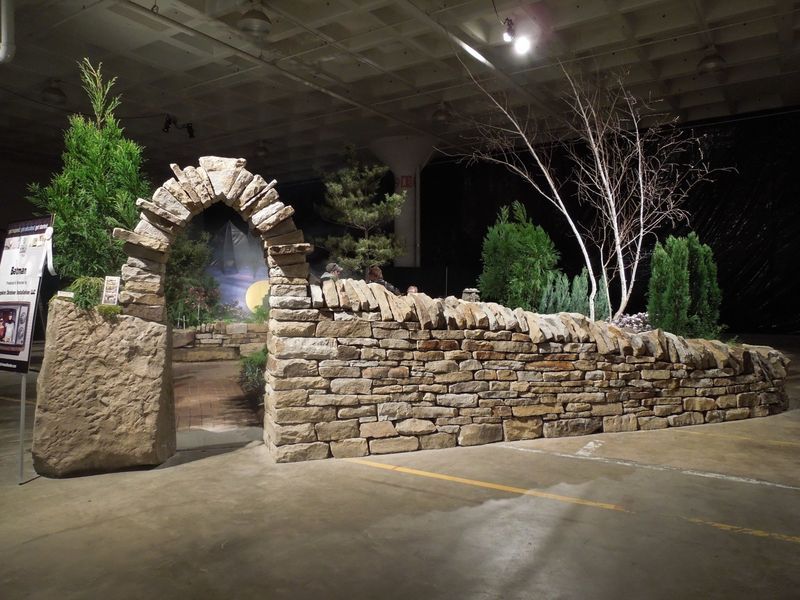 A stone wall in a parking lot with trees in the background