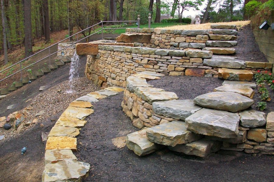 A stone wall with stairs and a fountain in the background