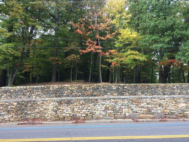A stone wall along the side of a road with trees in the background