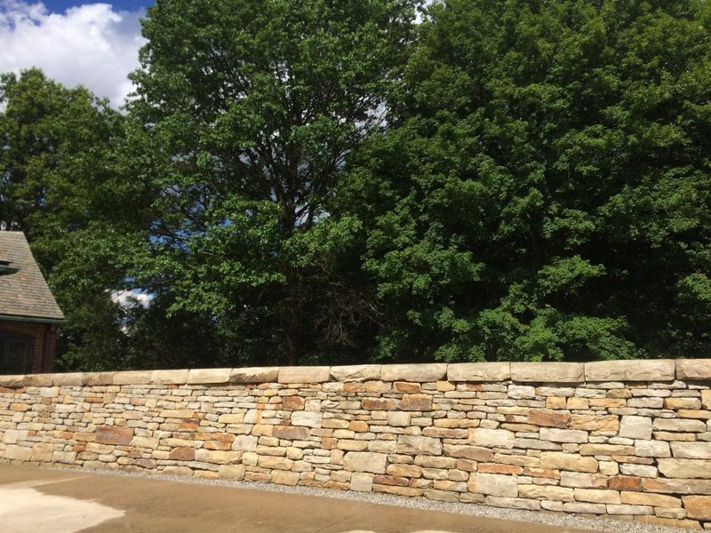A stone wall with trees in the background and a house in the background