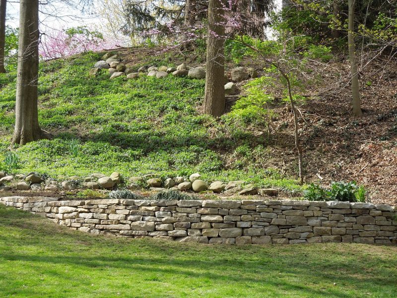 A stone wall surrounds a lush green hillside in a park.
