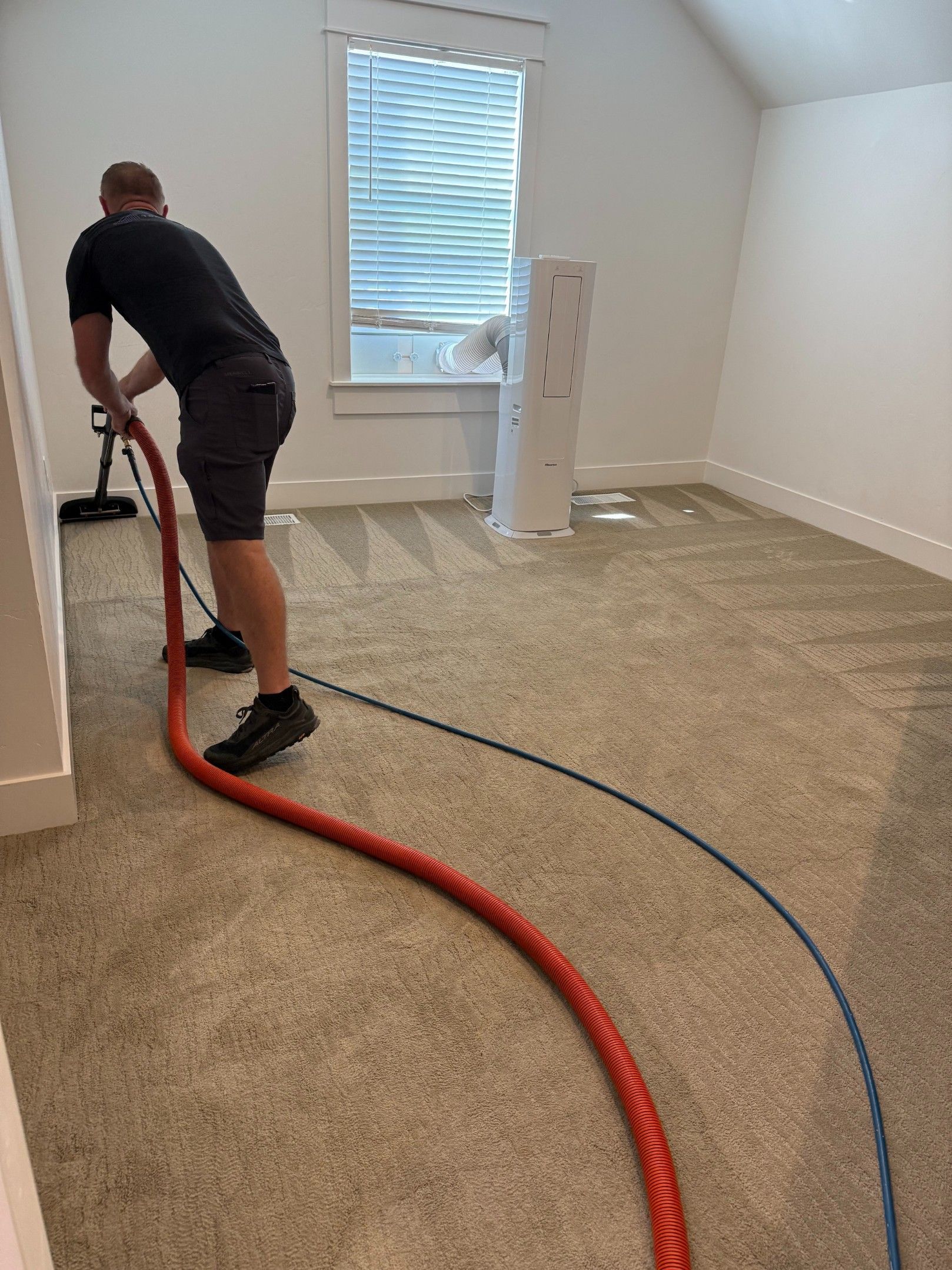Person vacuuming carpet in an empty room with a red hose and blue cord.