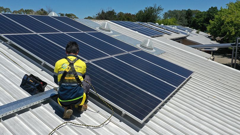 A man is installing solar panels on the roof of a building.