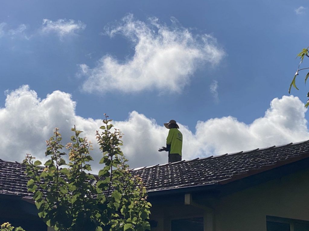 A man is standing on the roof of a house looking at the clouds.