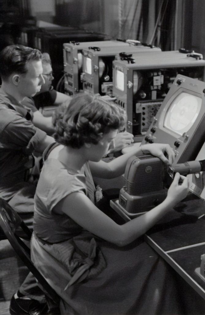 A black and white photo of a man and a woman working on a machine