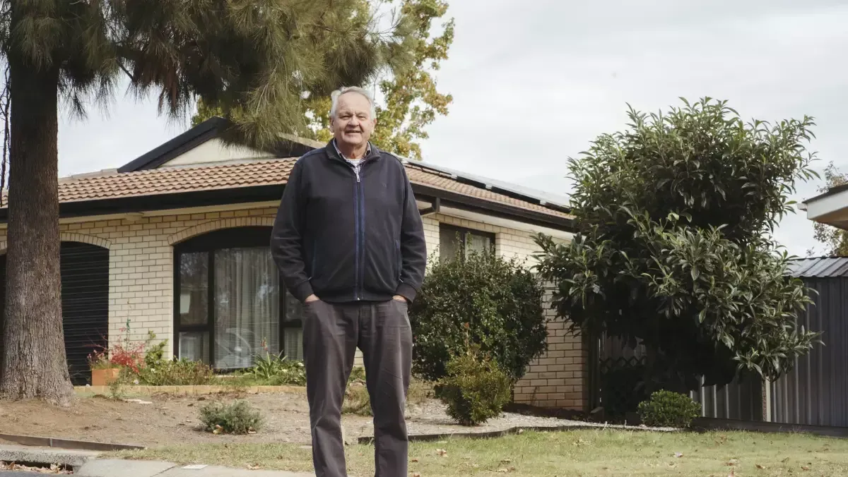 A man is standing in front of a house with his hands in his pockets.