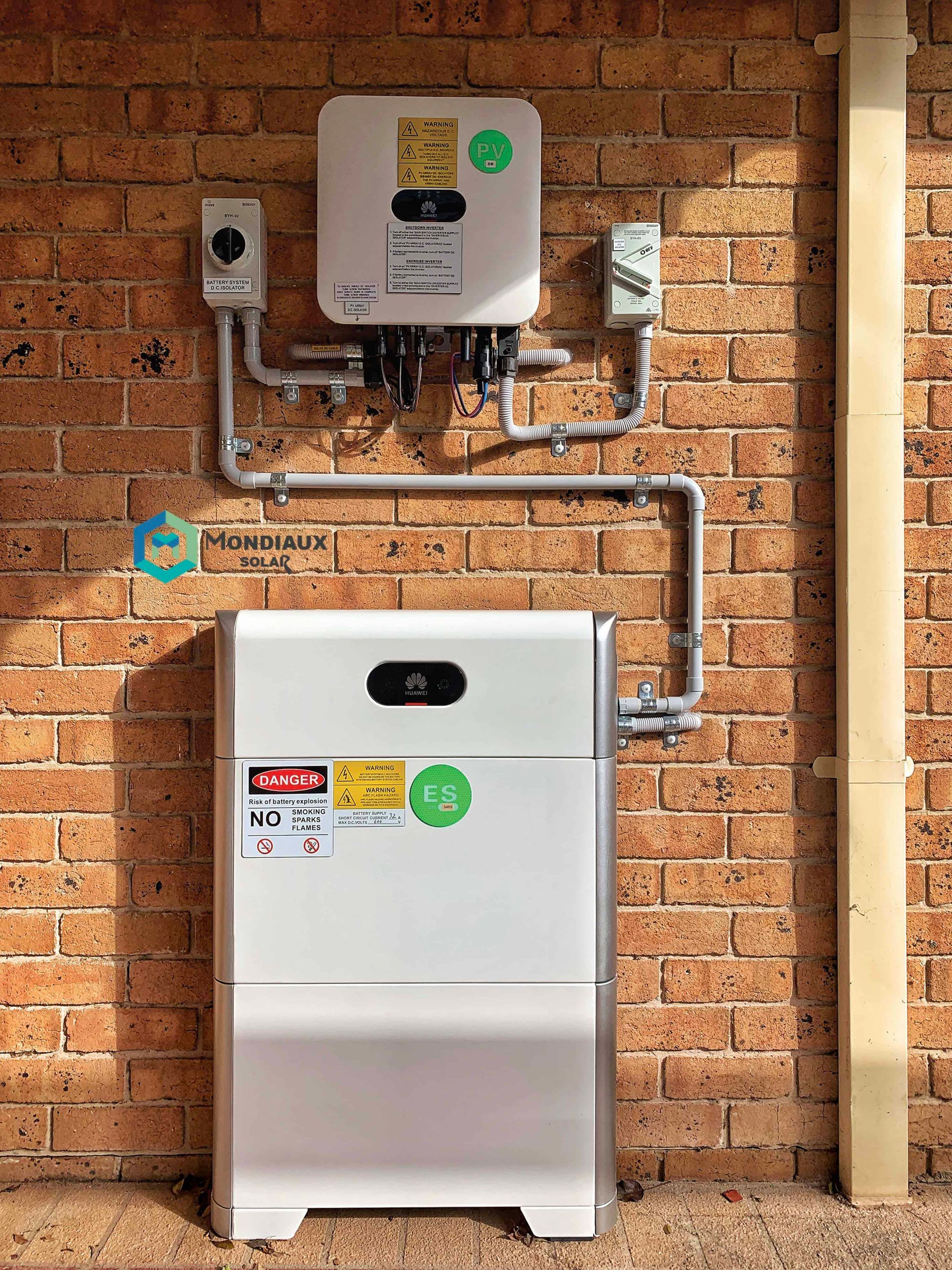 A white solar panel inverter and battery are mounted to a brick wall.