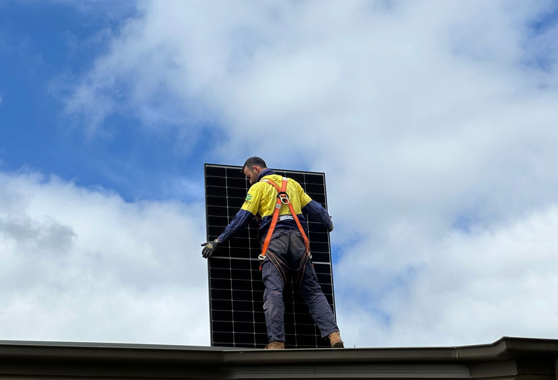 A man is standing on top of a roof holding a solar panel.