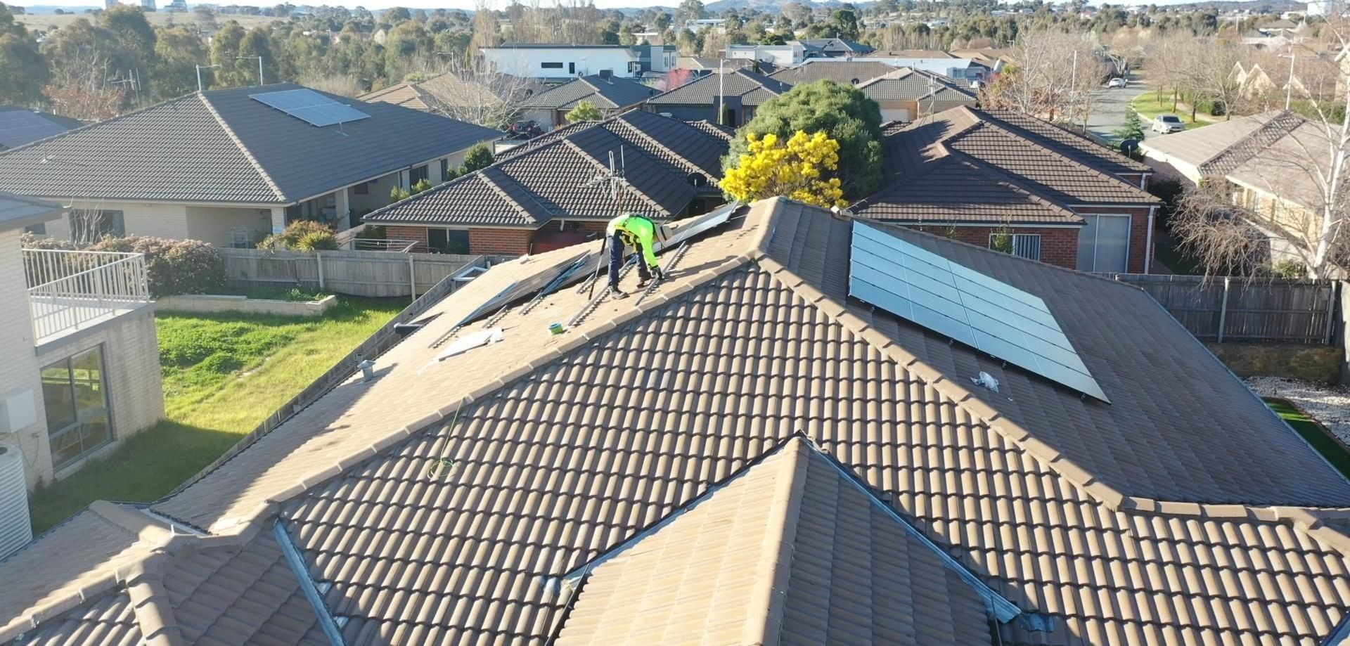 A man is working on the roof of a house with solar panels.