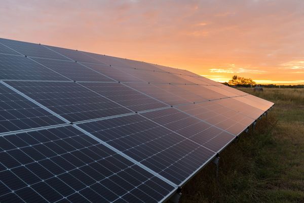 A row of solar panels in a field at sunset.