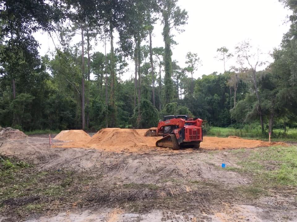 A bulldozer is moving dirt in a field with trees in the background.
