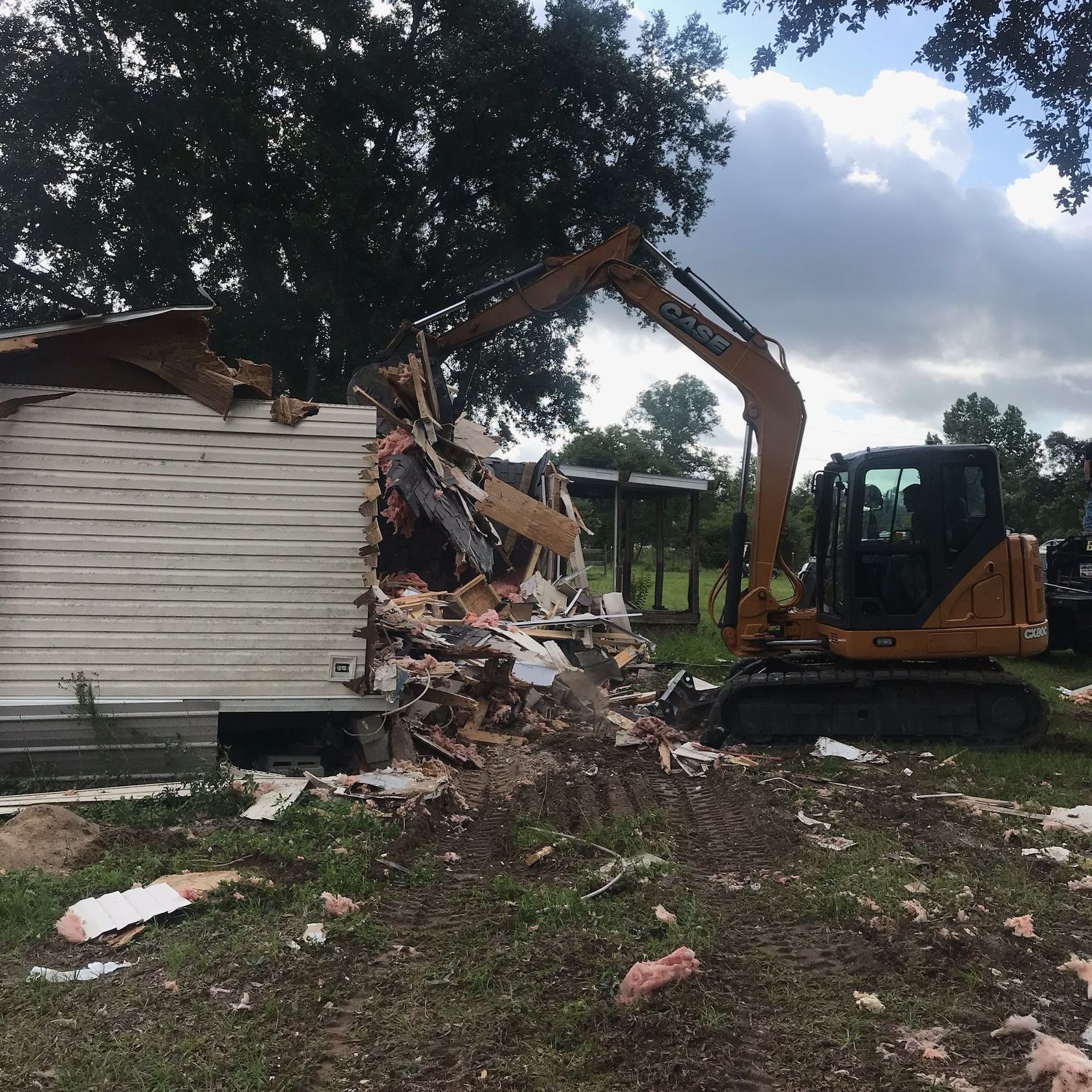 An excavator is demolishing a house in a field