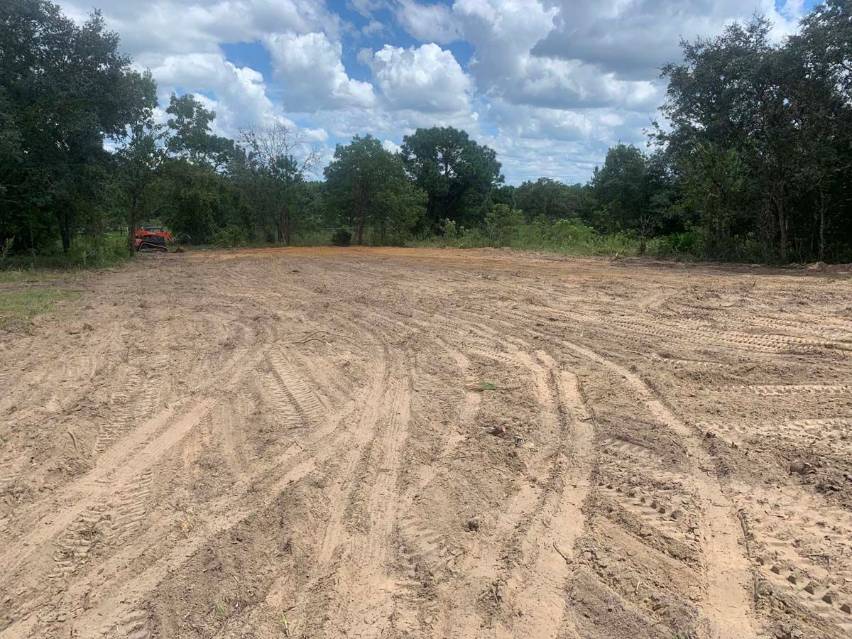 A dirt field with trees in the background and a tractor in the distance.