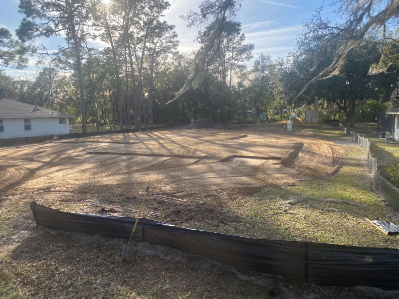 A large dirt field with trees in the background and a house in the background.