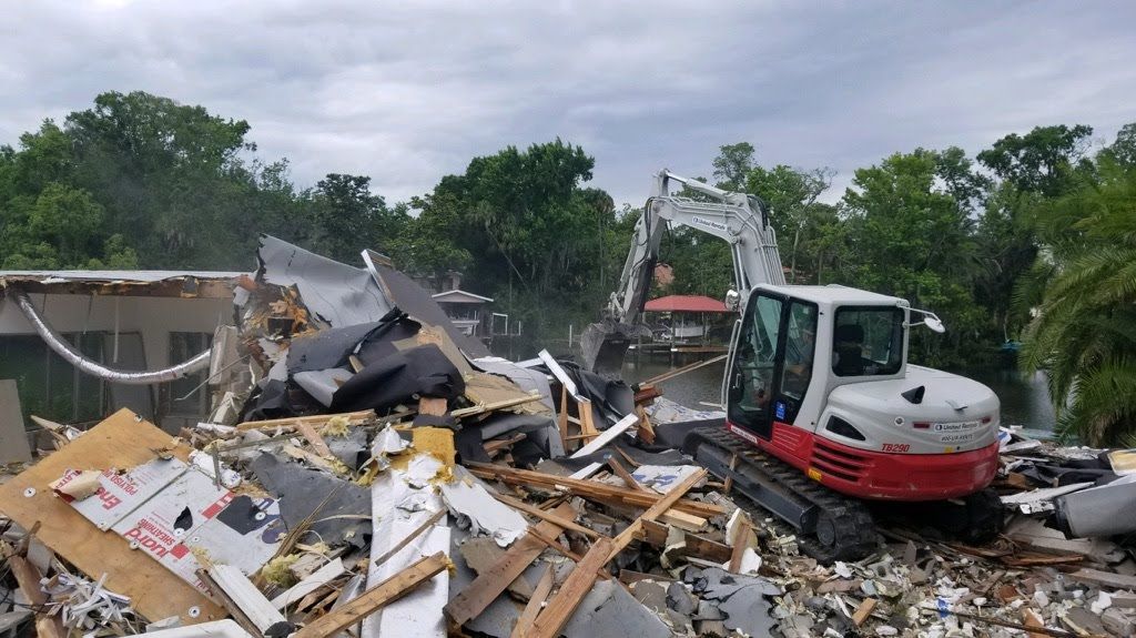A white and red excavator is demolishing a house.