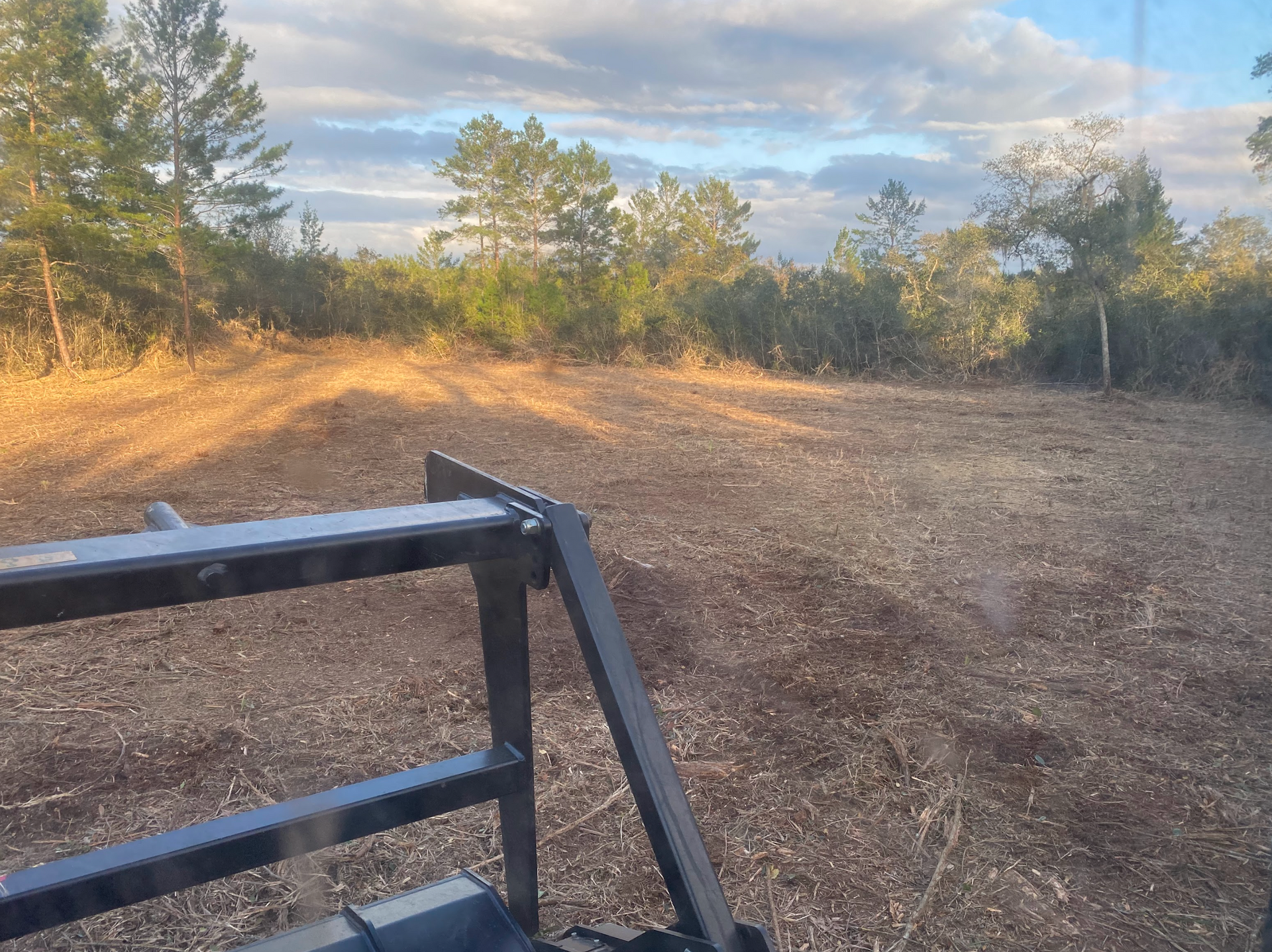 A person is driving a tractor through a field with trees in the background.