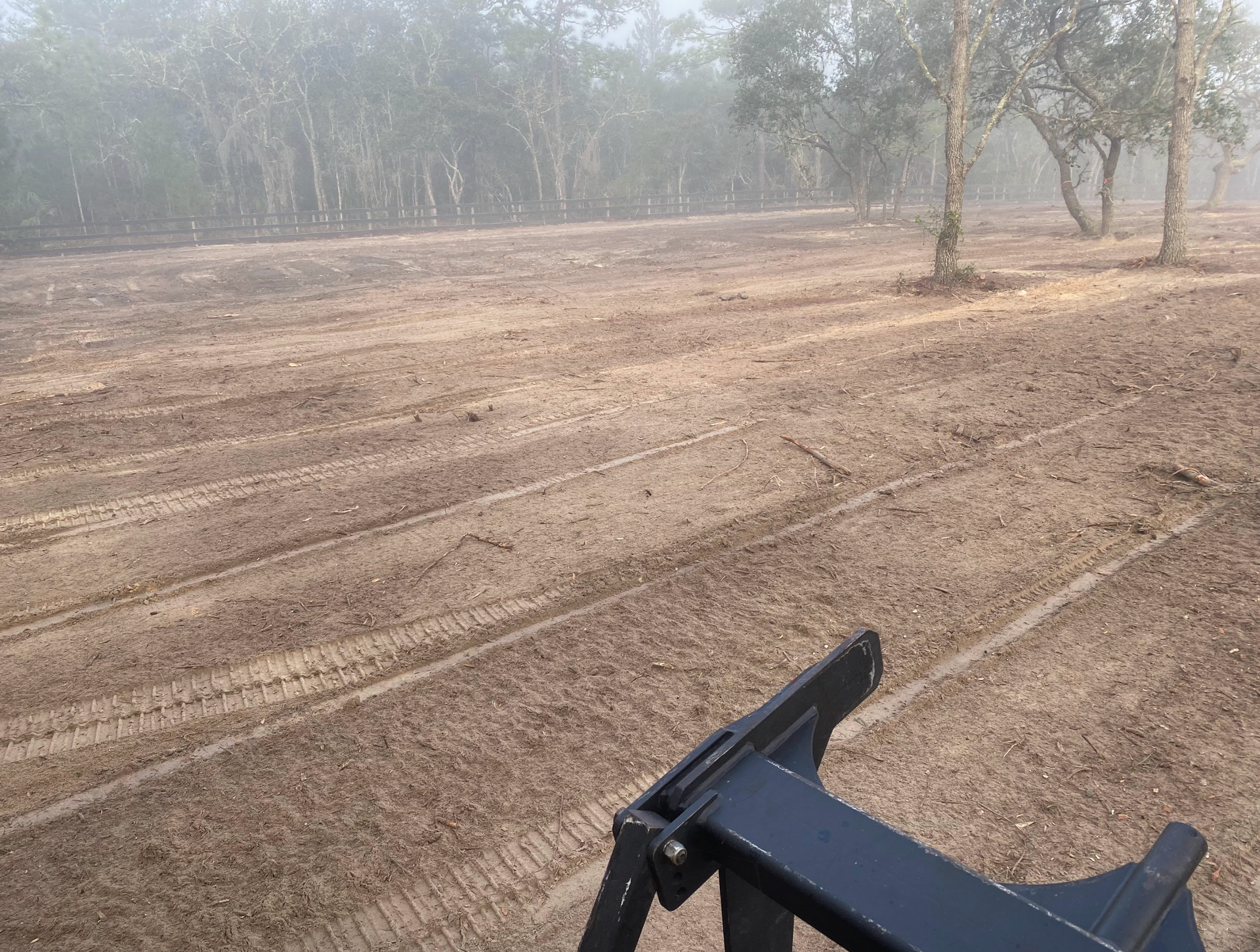 A large dirt field with trees in the background and a tractor in the foreground.