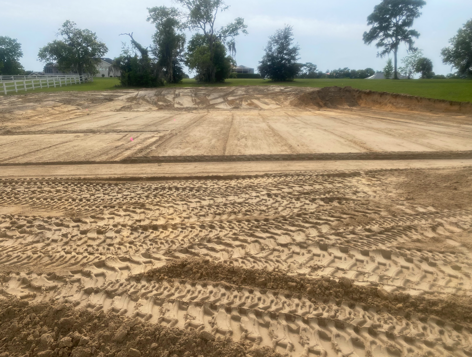 A dirt field with tire tracks in it and trees in the background