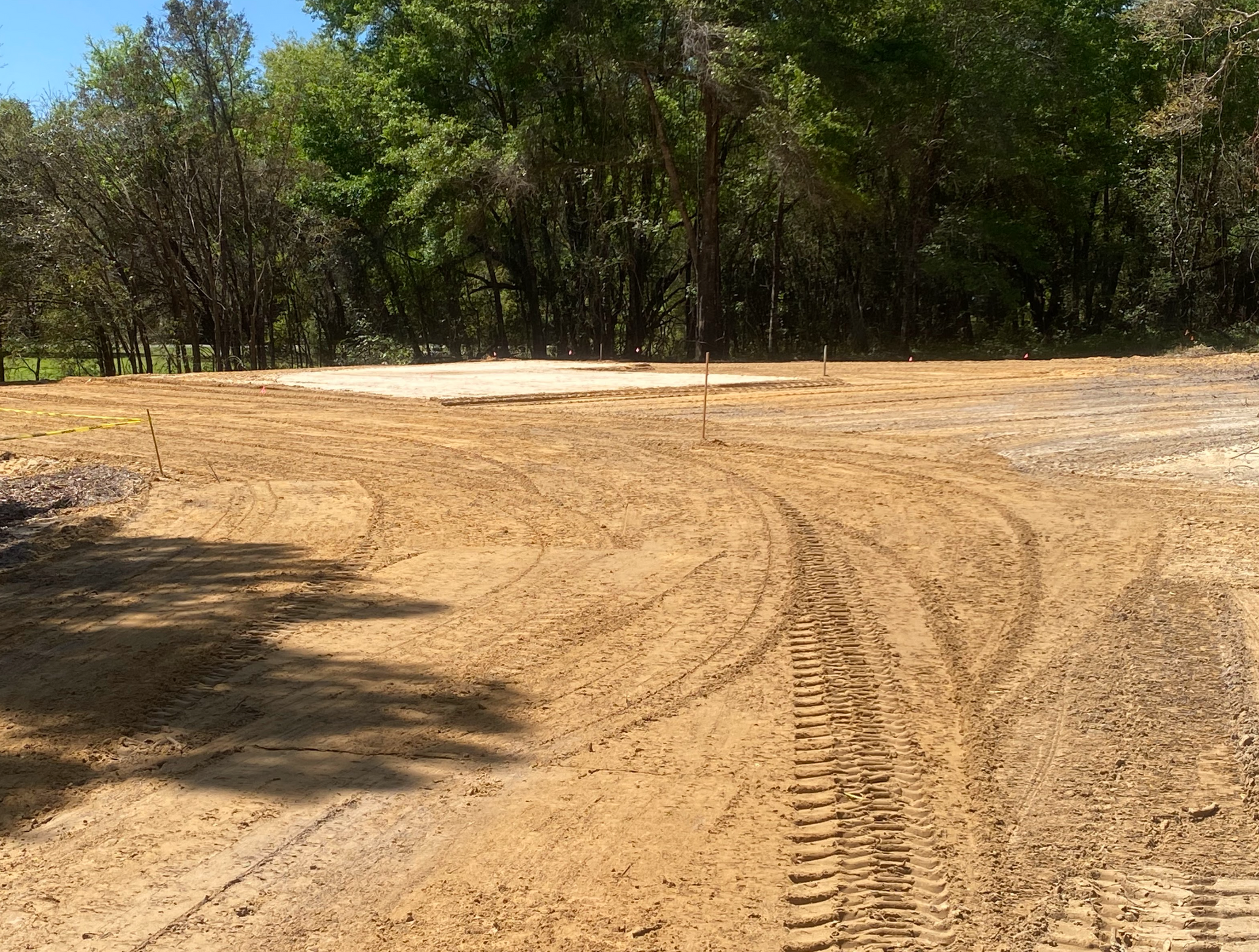 A dirt field with trees in the background and tire tracks in the dirt.