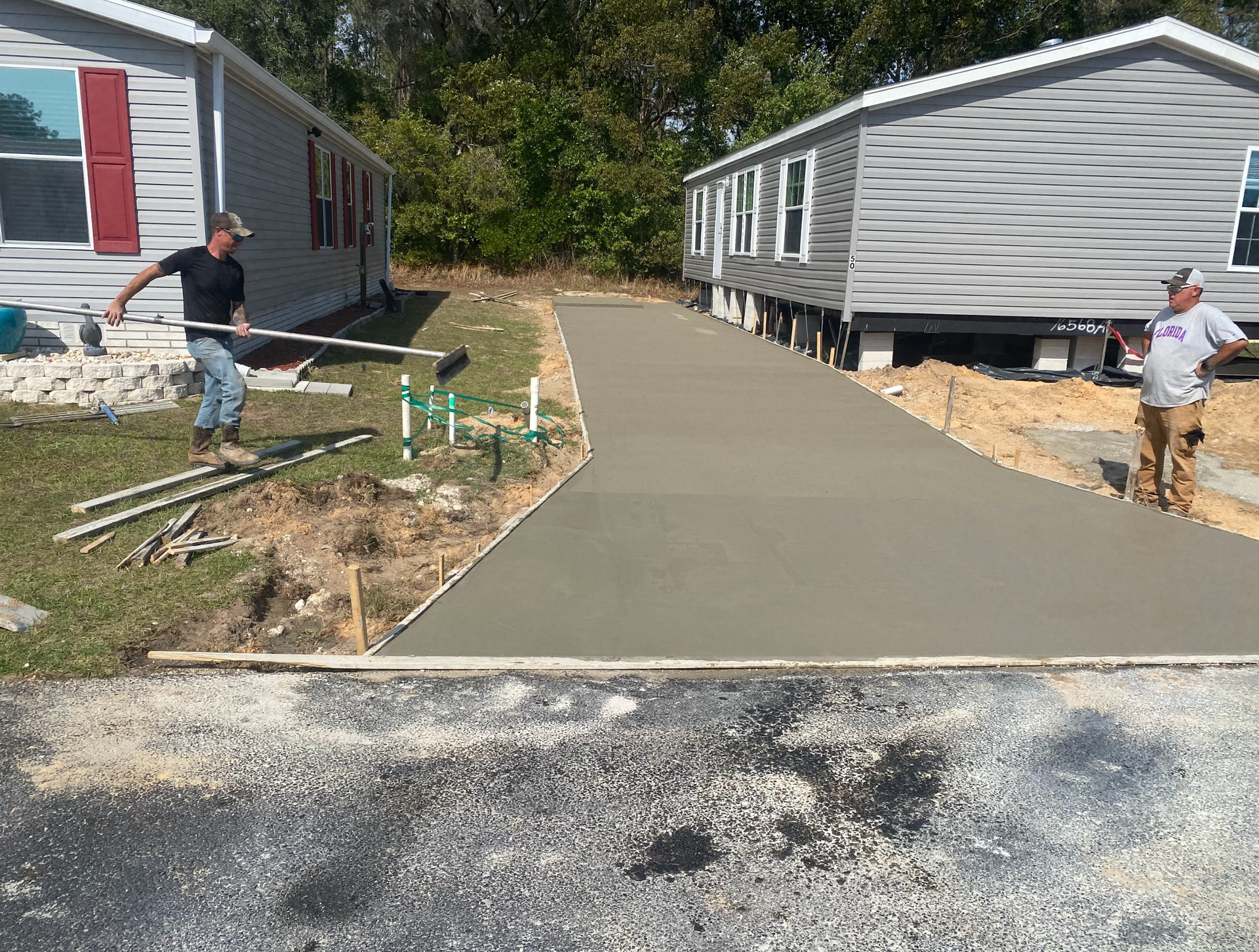 Two men are working on a concrete driveway in front of a mobile home.