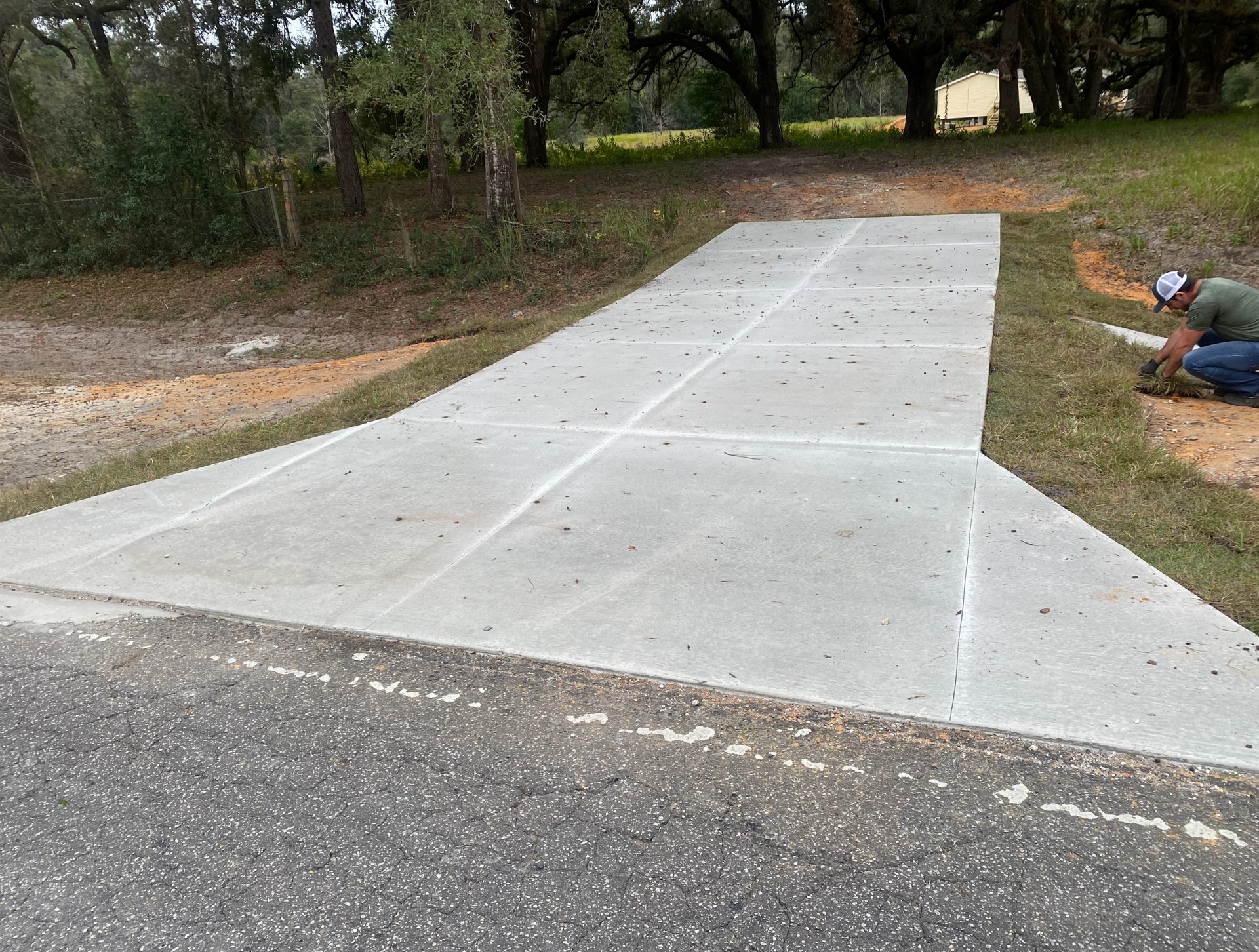 A man is working on a concrete driveway next to a road.