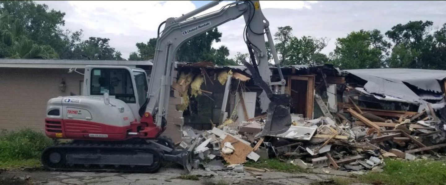 An excavator is demolishing a house in a field.