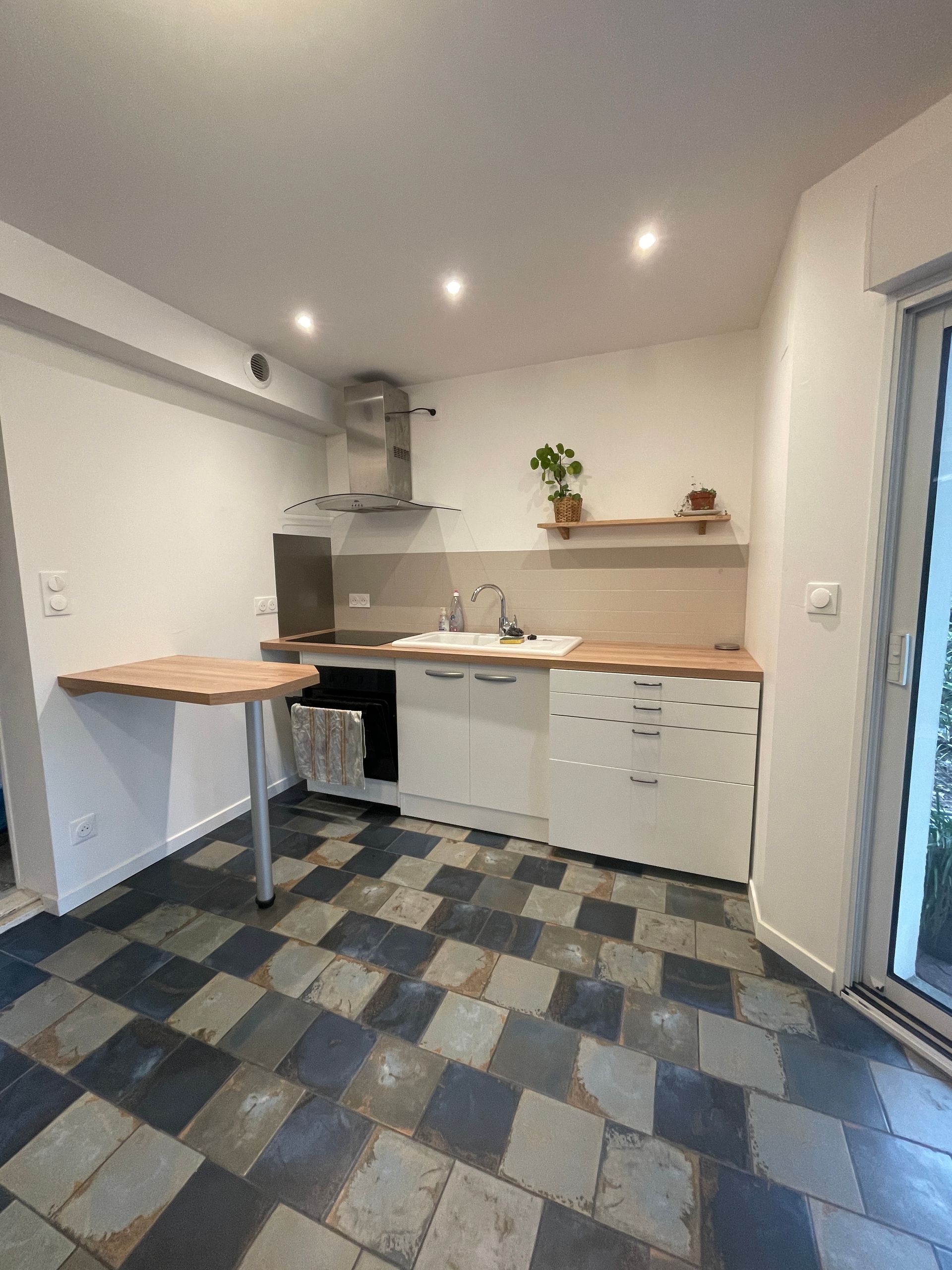 Cuisine avec armoires blanches, comptoirs en bois et table rabattable, et plancher à carreaux