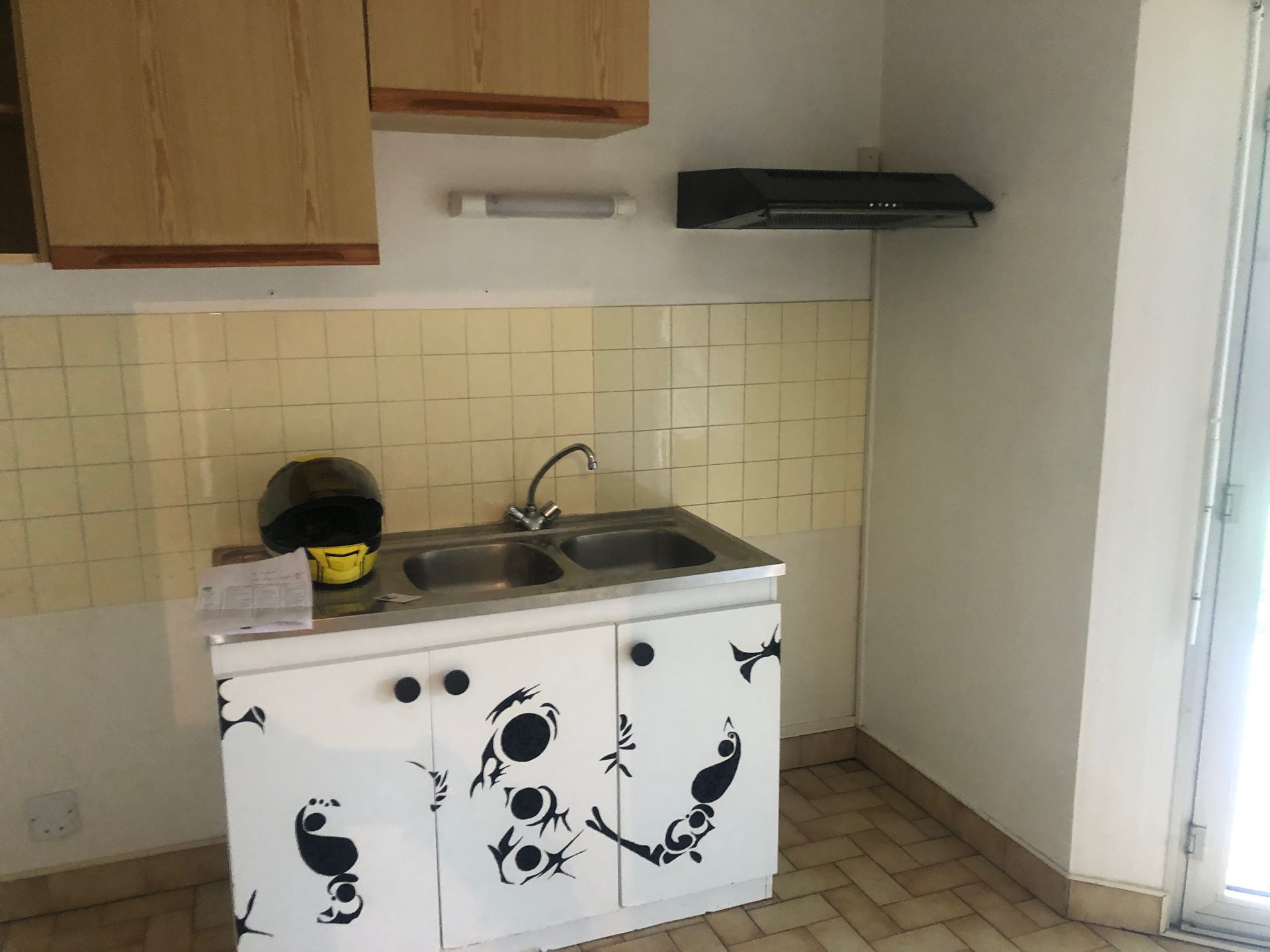 Petite cuisine avec un stickers sur les portes des placards, un évier, des placards suspendus et une hotte aspirante.