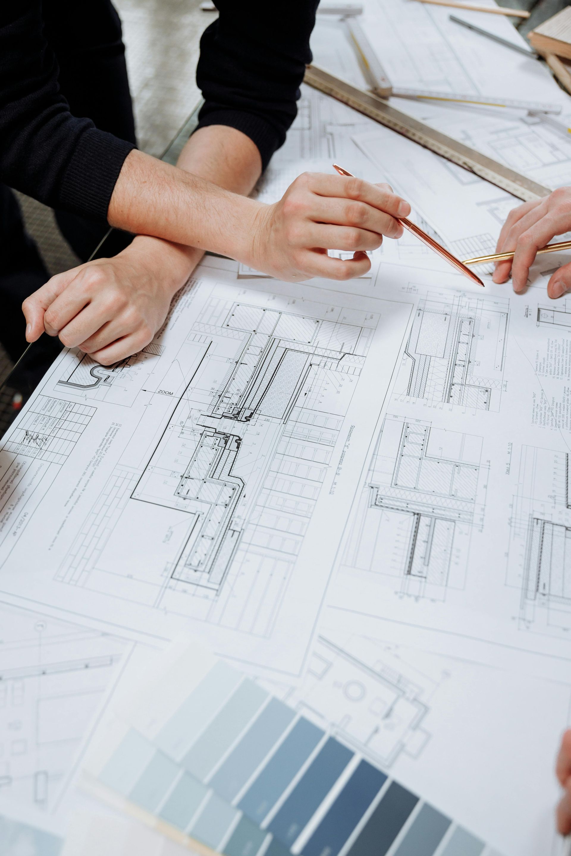 Des mains pointant vers des plans, discutant de plans architecturaux avec des échantillons de couleurs à proximité.