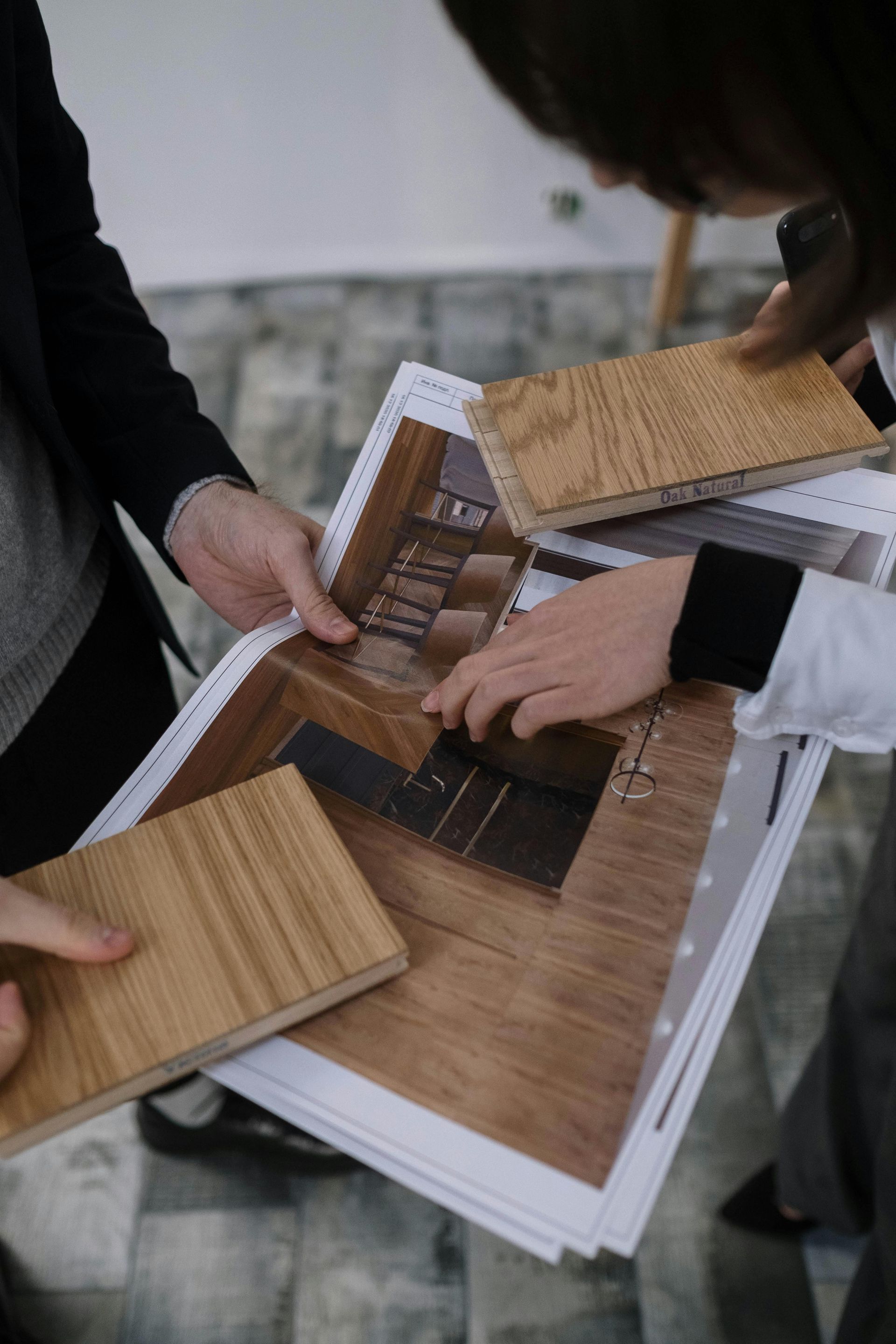 Trois collègues examinent des plans ensemble, assis à une table en bois dans un bureau. L'un d'eux porte un casque bleu.