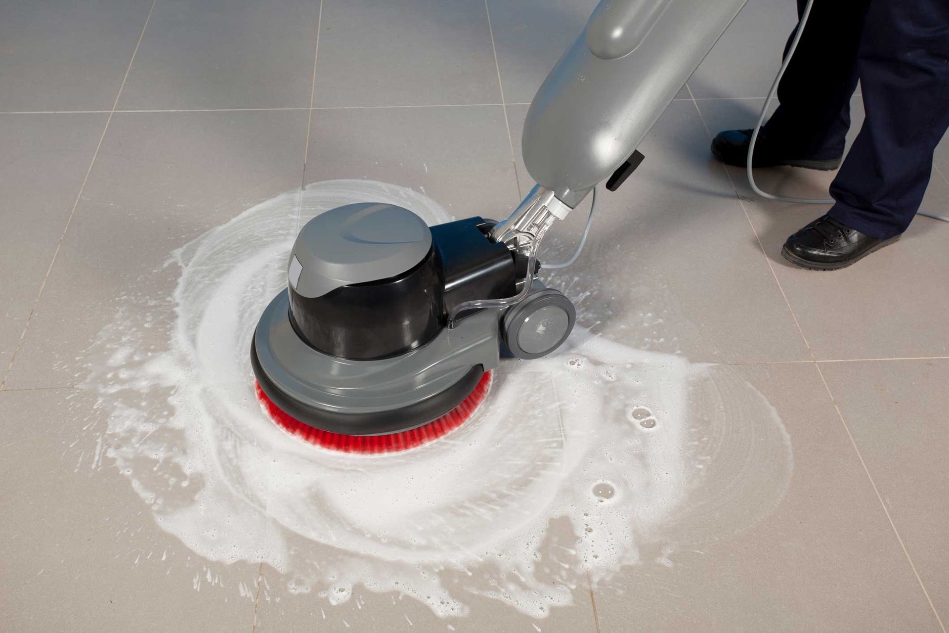 Floor scrubber machine cleaning a tiled floor with soapy water.
