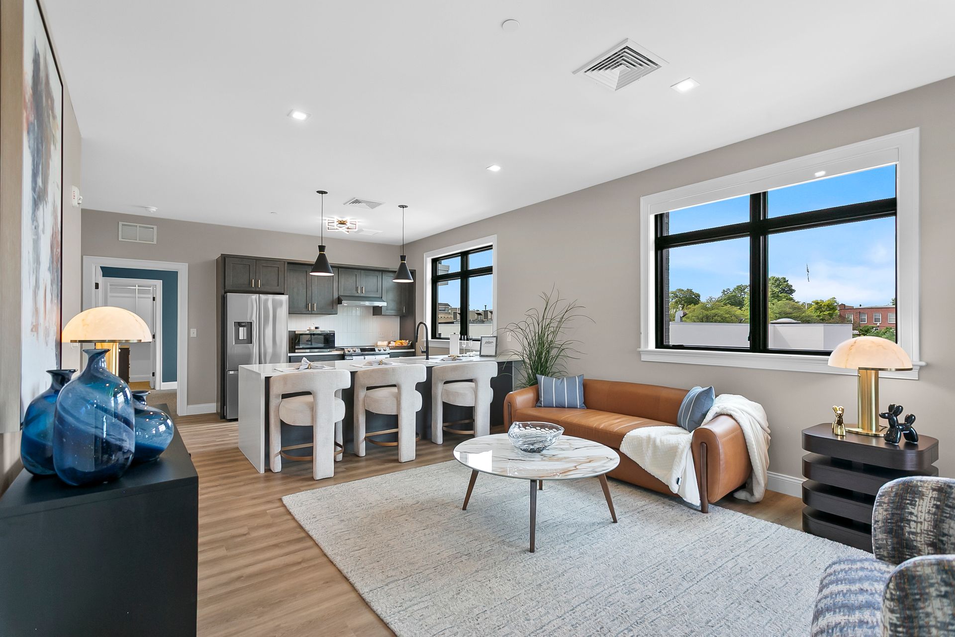 Modern open-plan living room and kitchen with white walls, wood floors, gray sofa, and large windows