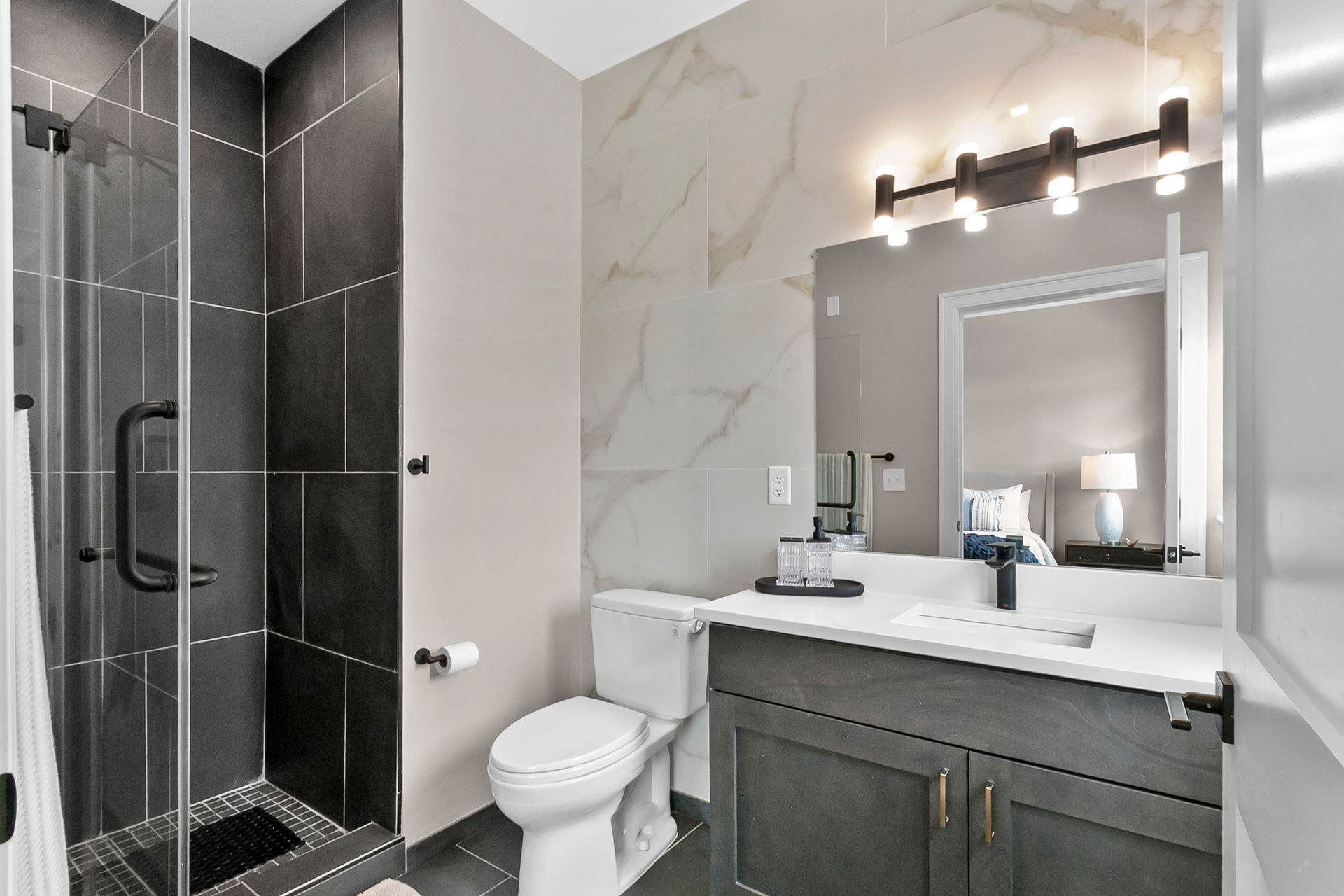 Modern bathroom with glass shower, gray vanity, white toilet, and marble-look walls