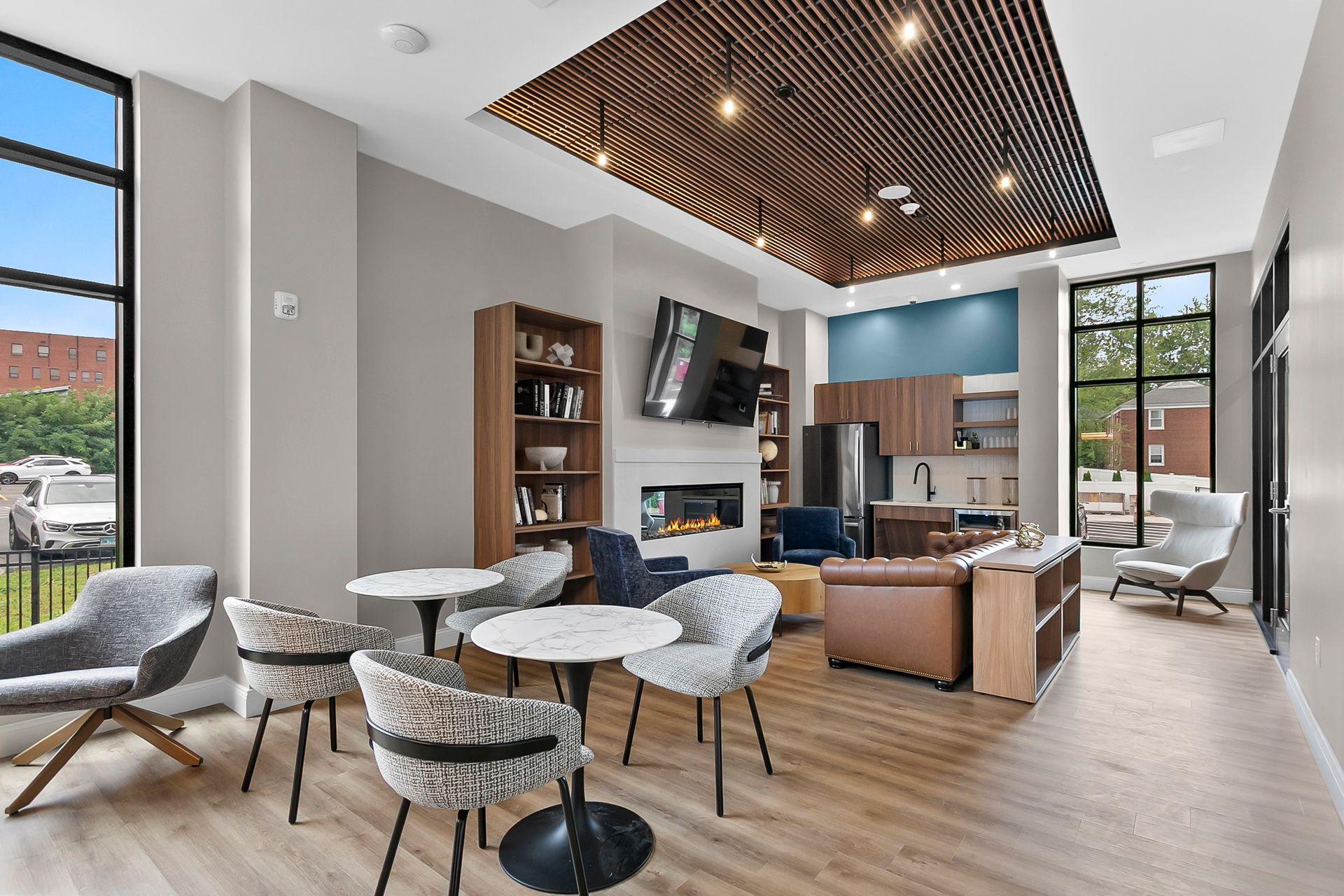 Modern open-plan living room with dining table, gray chairs, wood ceiling, and large windows