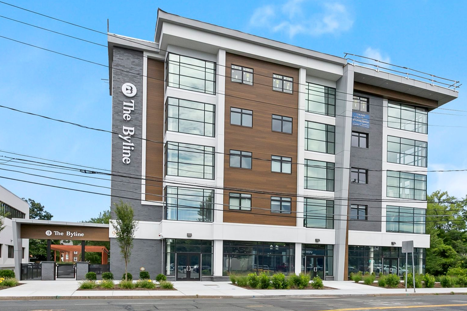 Modern four-story building with glass windows, brown and gray facade, and a street-side entrance