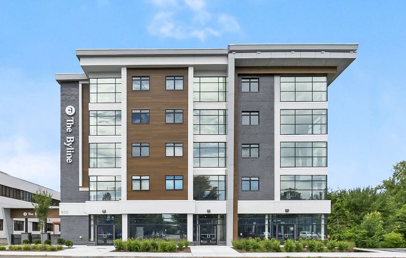 Modern multi-story building with gray and brown facade, large windows, and a blue sky backdrop