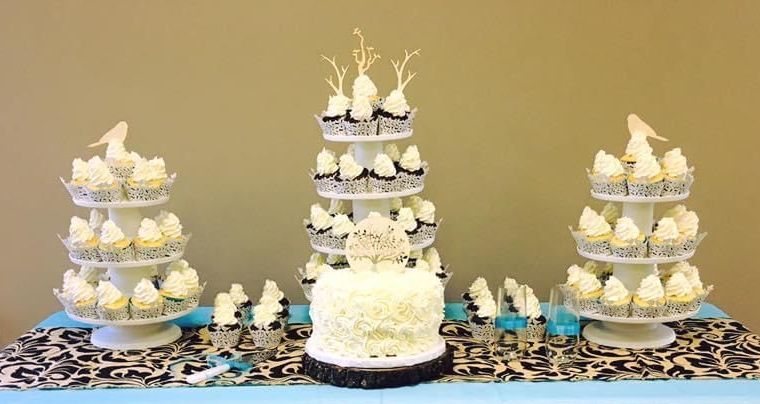 Cupcake display with a central cake. Cupcakes are on tiered stands with white frosting and black liners.