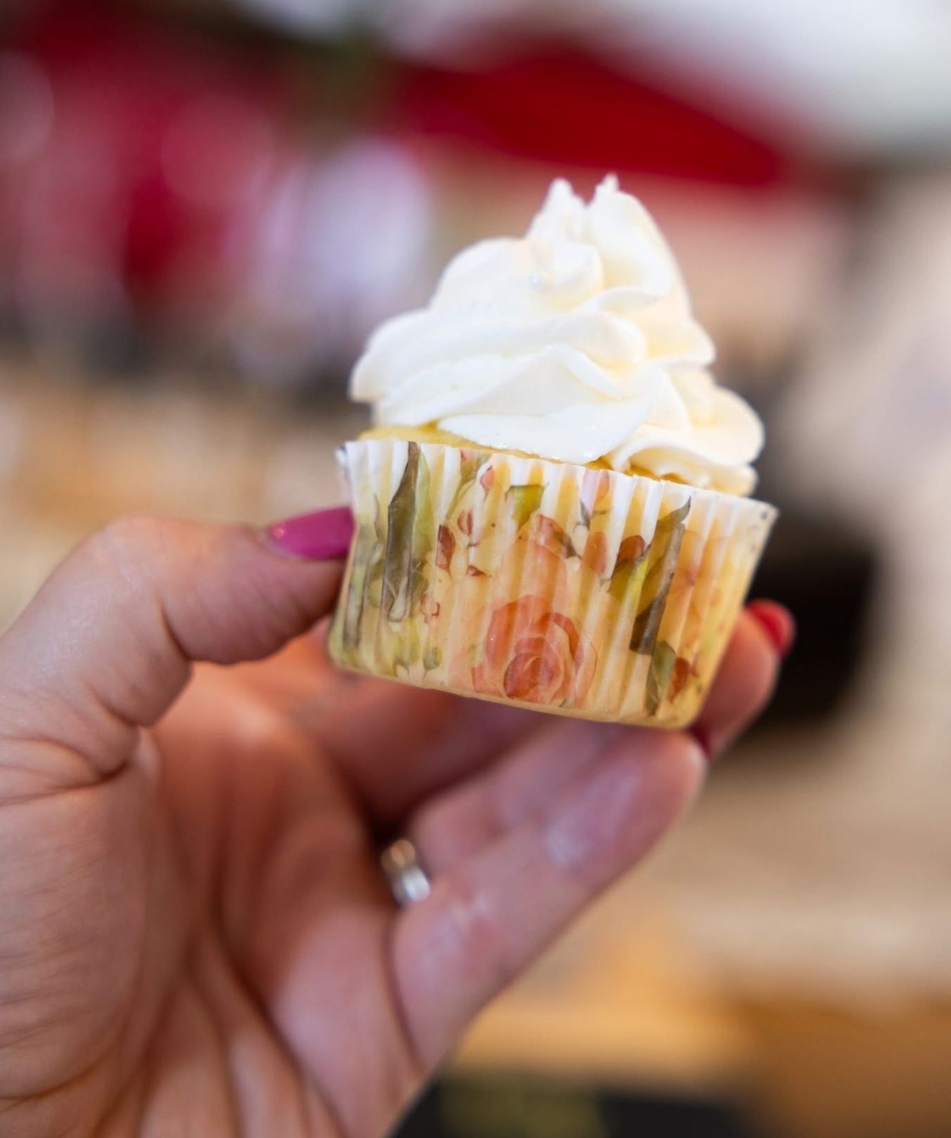 Hand holding a cupcake with white frosting and a floral patterned wrapper.