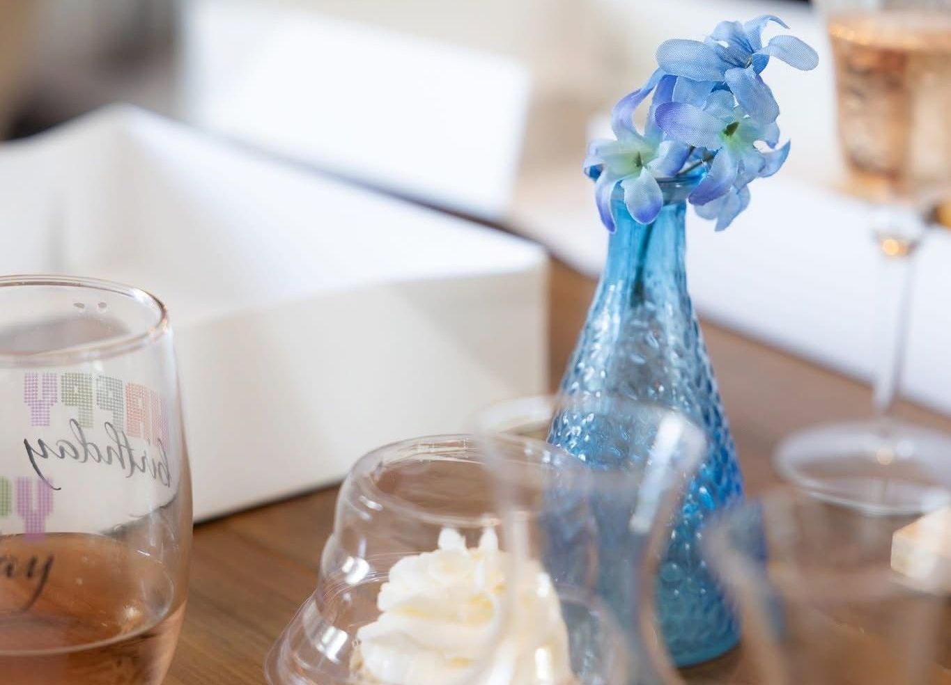 Blue flowers in a small blue vase on a table with glassware and a birthday glass.