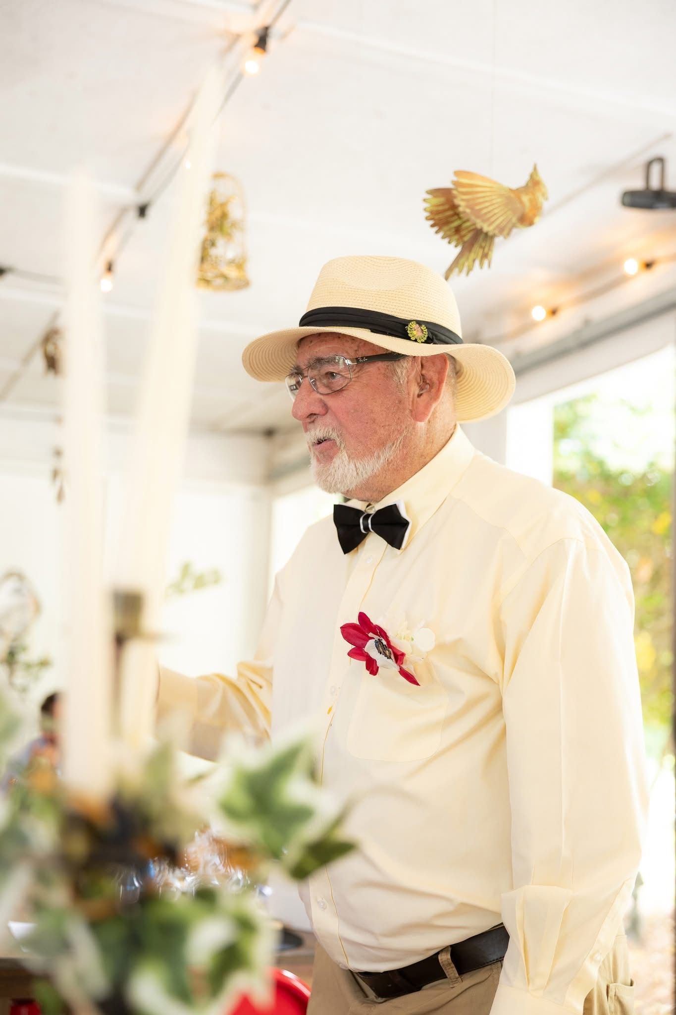 Man in straw hat and bow tie adjusts a table centerpiece.