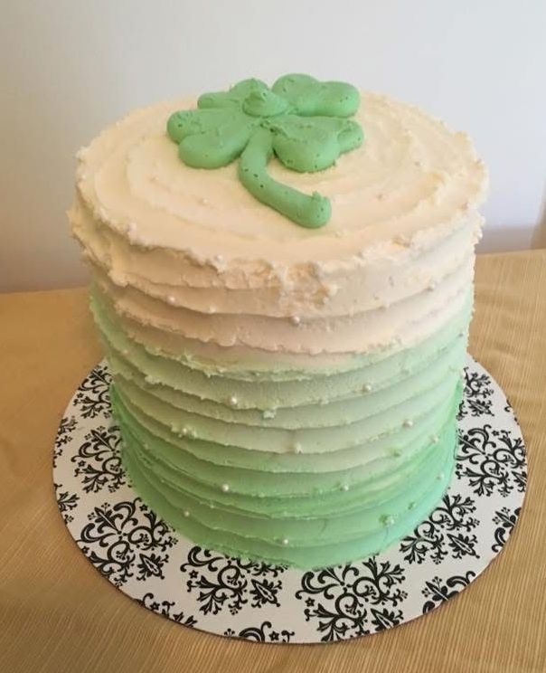 St. Patrick's Day cake with green ombre frosting and a shamrock on top, on a patterned cake board.