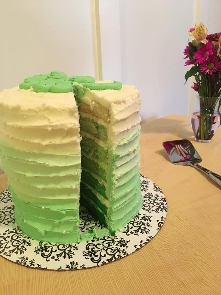Green ombre cake decorated with a shamrock, cut to reveal layers. On a decorative platter.