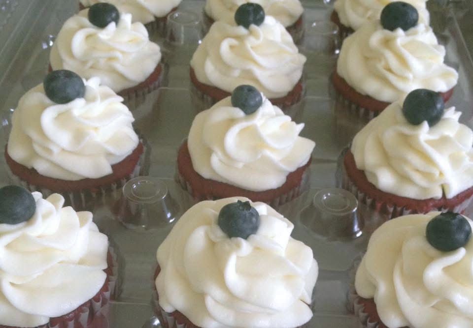 Red velvet cupcakes with white frosting and blueberries in a plastic container.