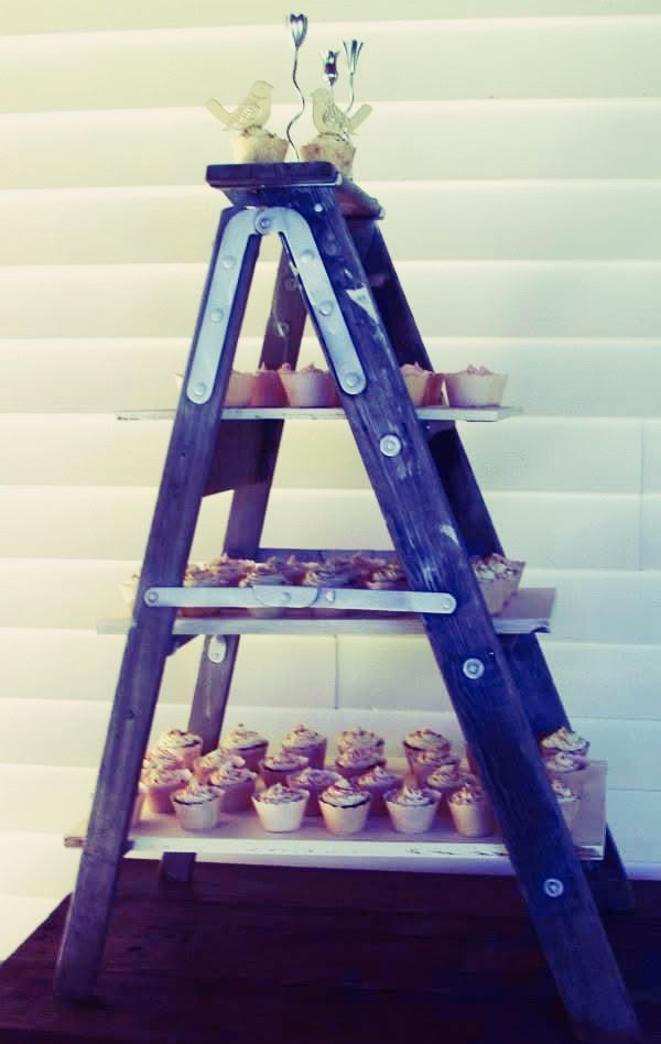 Cupcakes on a rustic wooden ladder display against a white slatted background.