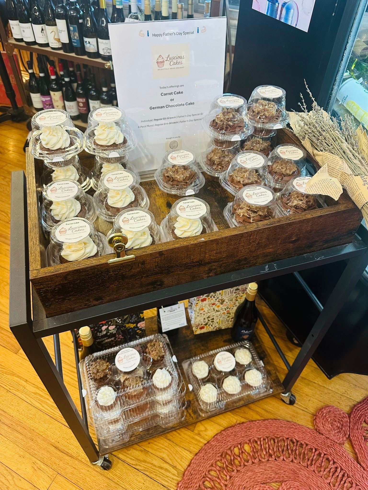 A wooden cart displays packaged baked goods for sale, in a store with wine bottles.