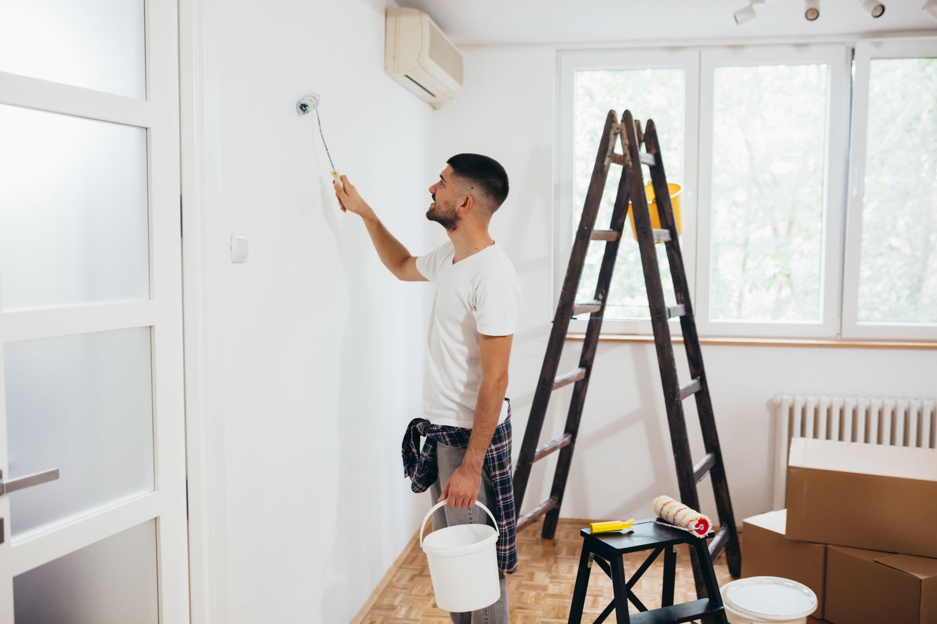 A man is painting a wall in a room with a ladder.
