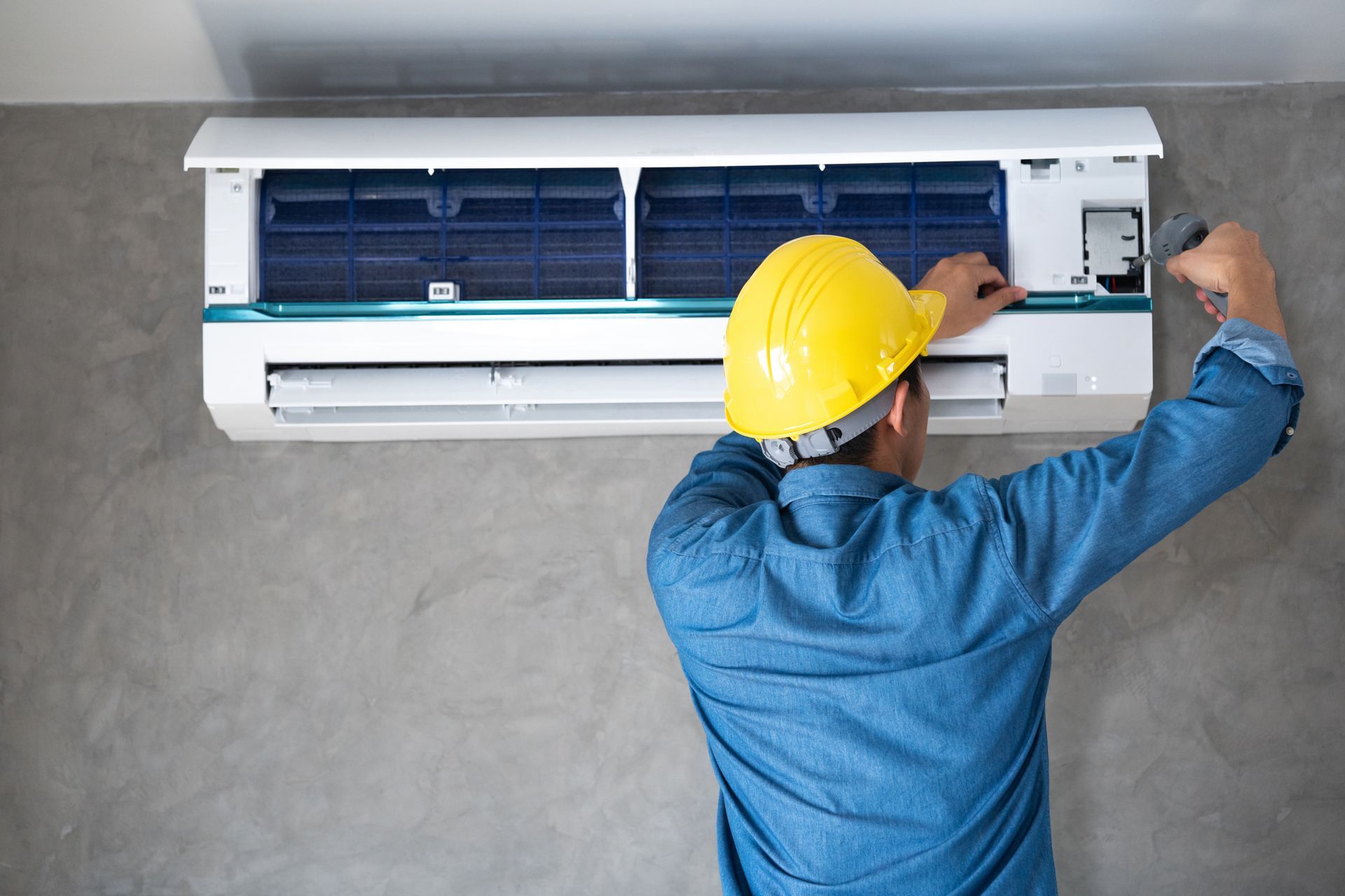 A man wearing a hard hat is working on an air conditioner.