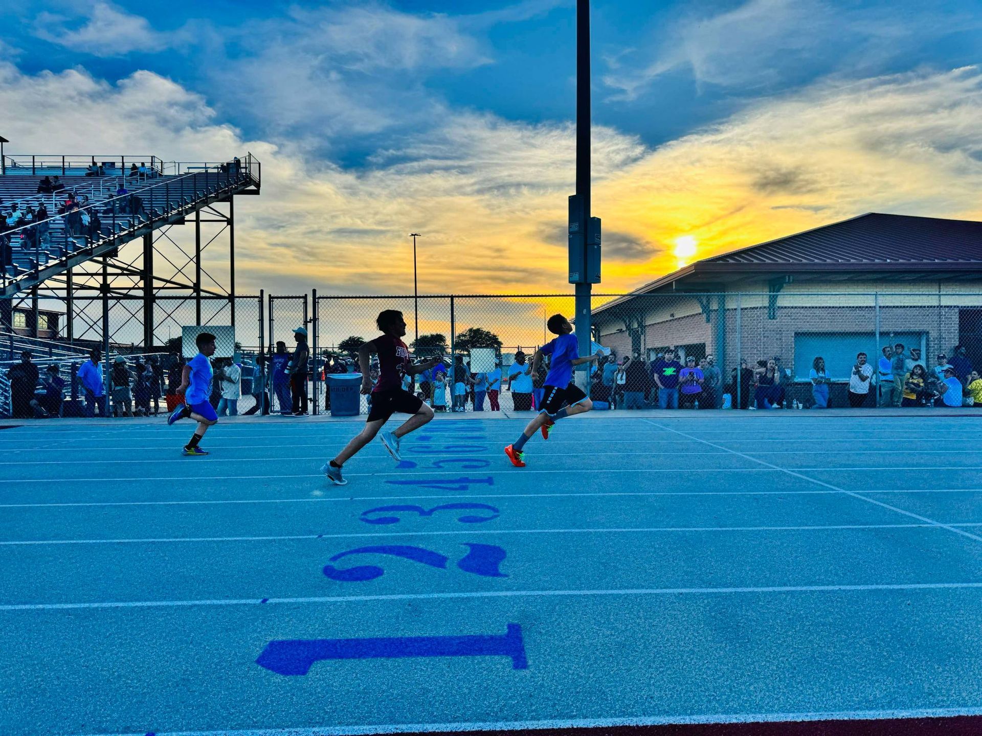 A person wearing a hat and orange shirt, holding a baseball bat on their shoulder on a baseball field.