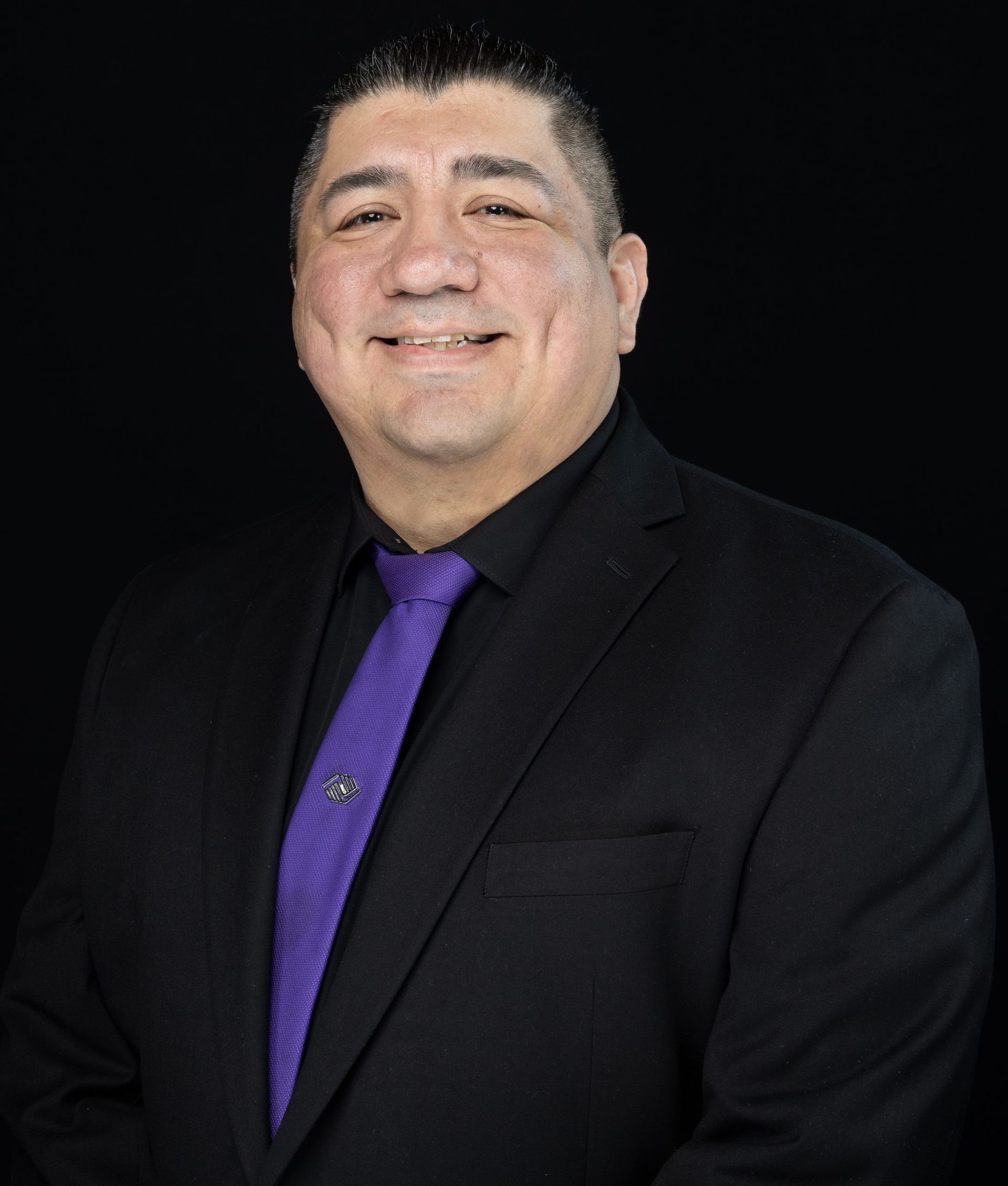 Man in green polo stands on a football field, arms crossed, stadium in background.